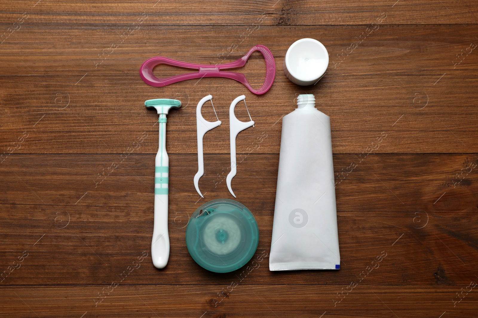 Photo of Different tongue cleaners, dental floss and toothpaste on wooden table, flat lay