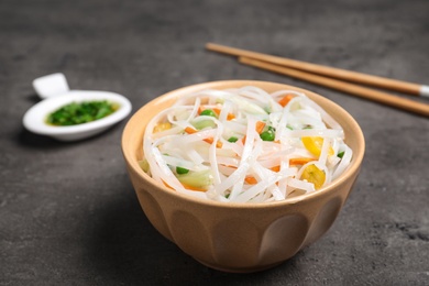 Photo of Bowl of rice noodles with vegetables and chopsticks on grey background