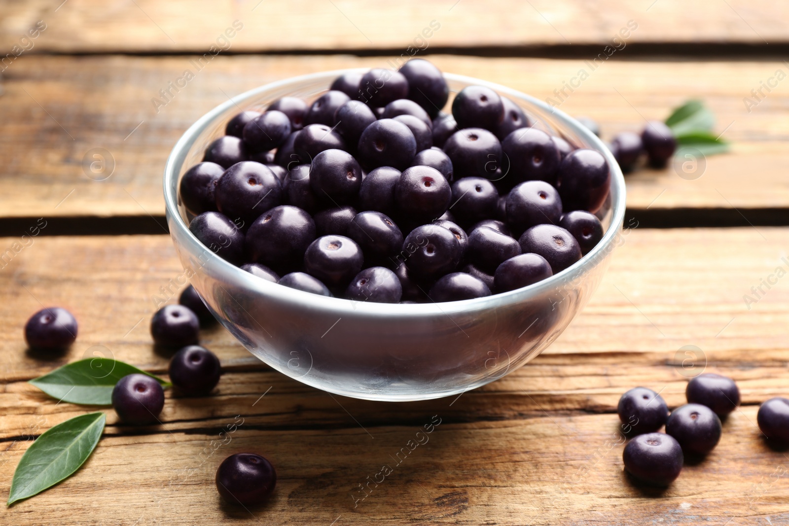 Photo of Fresh acai berries in glass bowl on wooden table, closeup