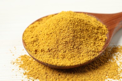 Photo of Curry powder in spoon on white wooden table, closeup