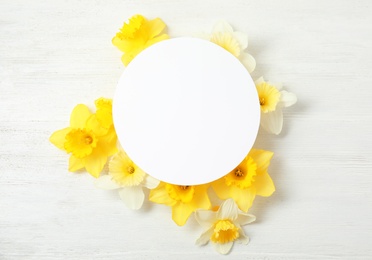 Photo of Flat lay composition with daffodils and card on white wooden background, space for text. Fresh spring flowers