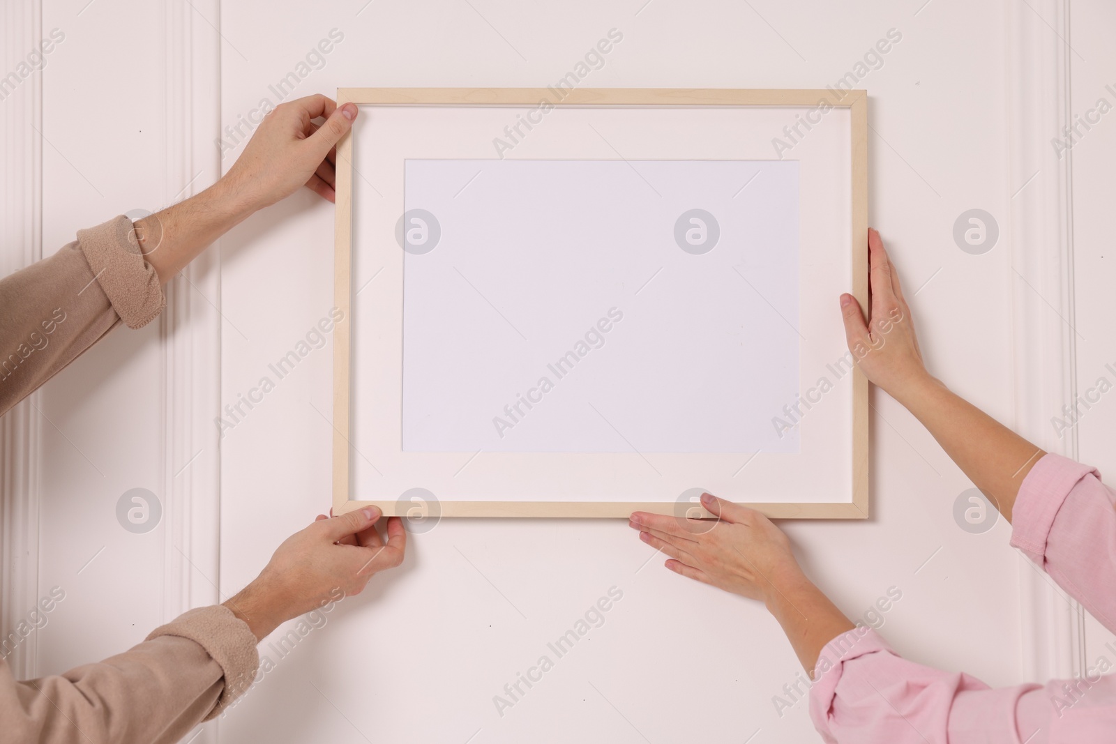 Photo of Man and woman hanging picture frame on white wall, closeup