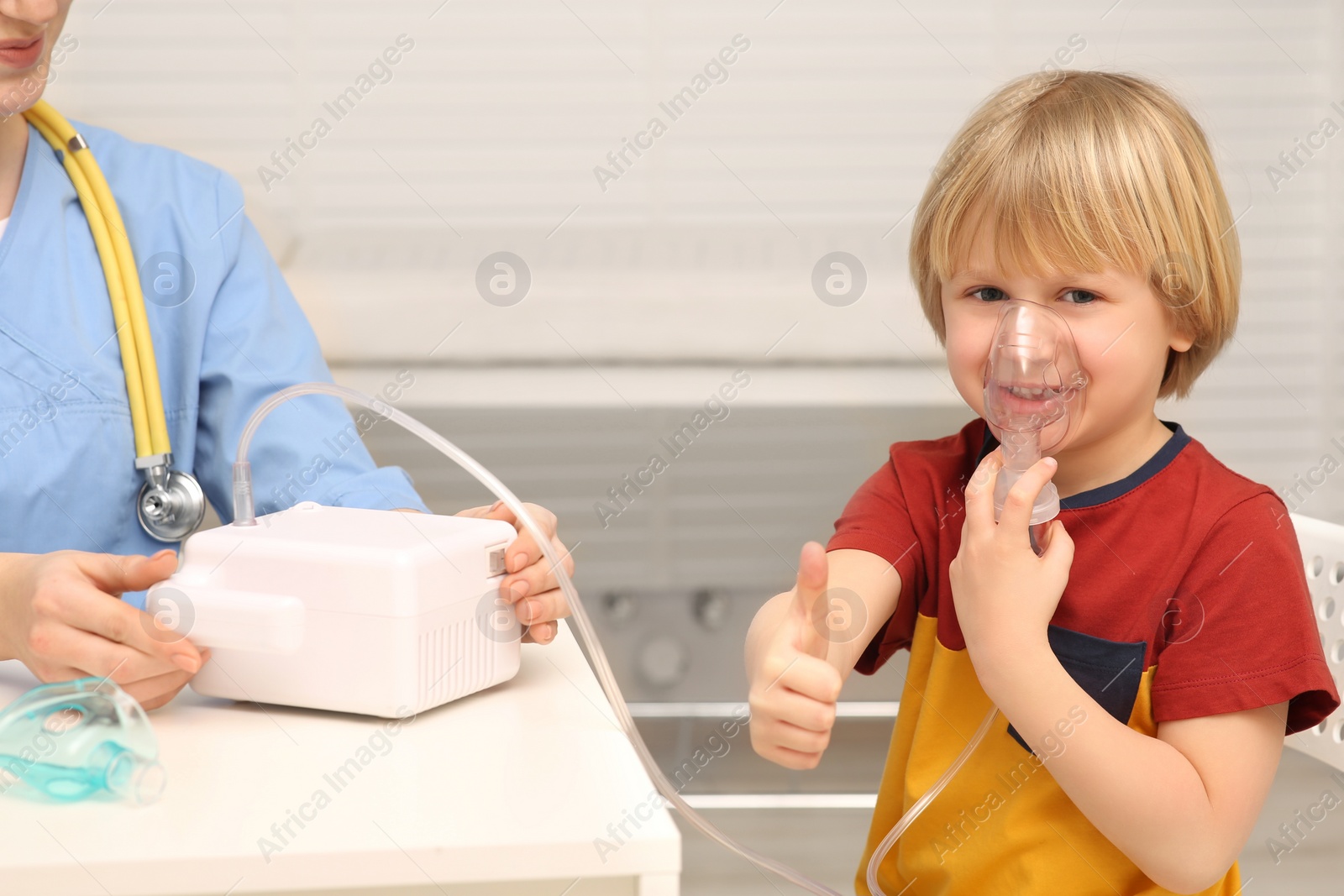 Photo of Little boy showing thumbs up while using nebulizer for inhalation in hospital