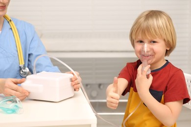 Photo of Little boy showing thumbs up while using nebulizer for inhalation in hospital