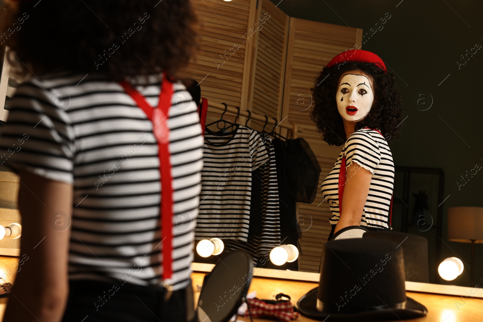 Photo of Young woman in mime costume posing near mirror indoors