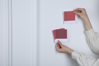 Photo of Woman with color sample cards choosing paint shade near white wall, closeup. Interior design