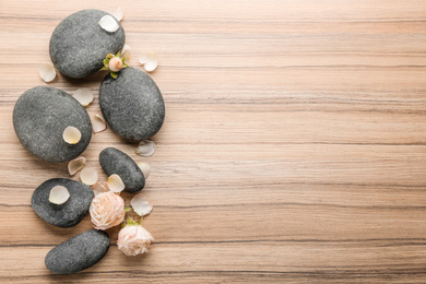 Stones and rose flowers on wooden background, top view with space for text. Zen lifestyle