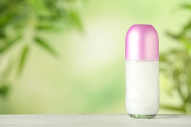 Photo of Deodorant container on white wooden table against blurred background. Space for text