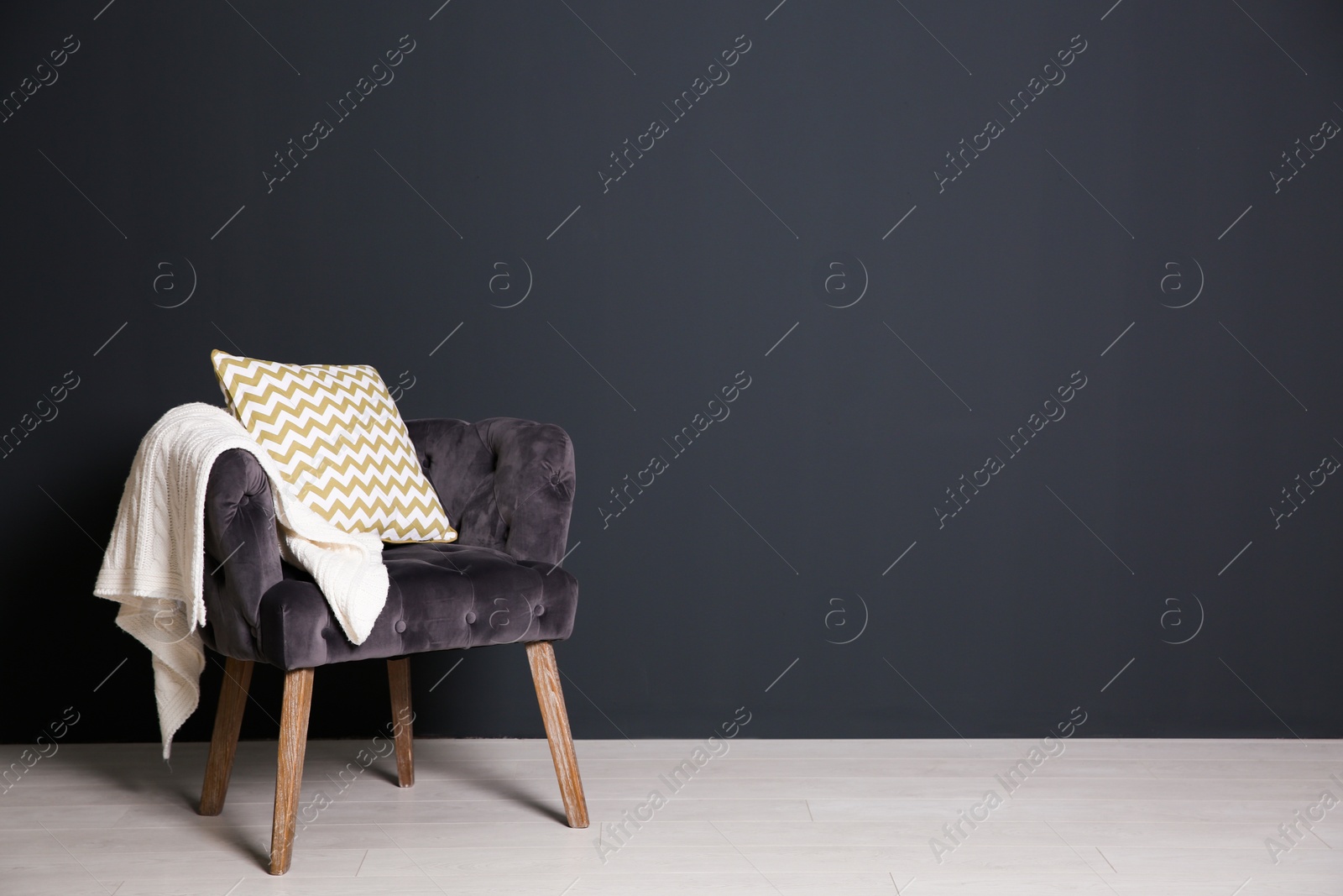 Photo of Stylish armchair with pillow and plaid near dark wall, space for text. Interior design