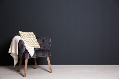 Photo of Stylish armchair with pillow and plaid near dark wall, space for text. Interior design