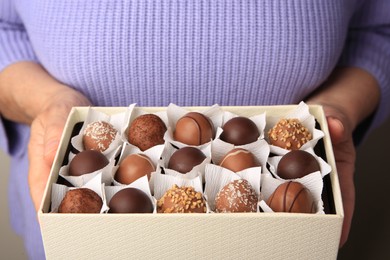 Photo of Woman holding box of delicious chocolate candies, closeup