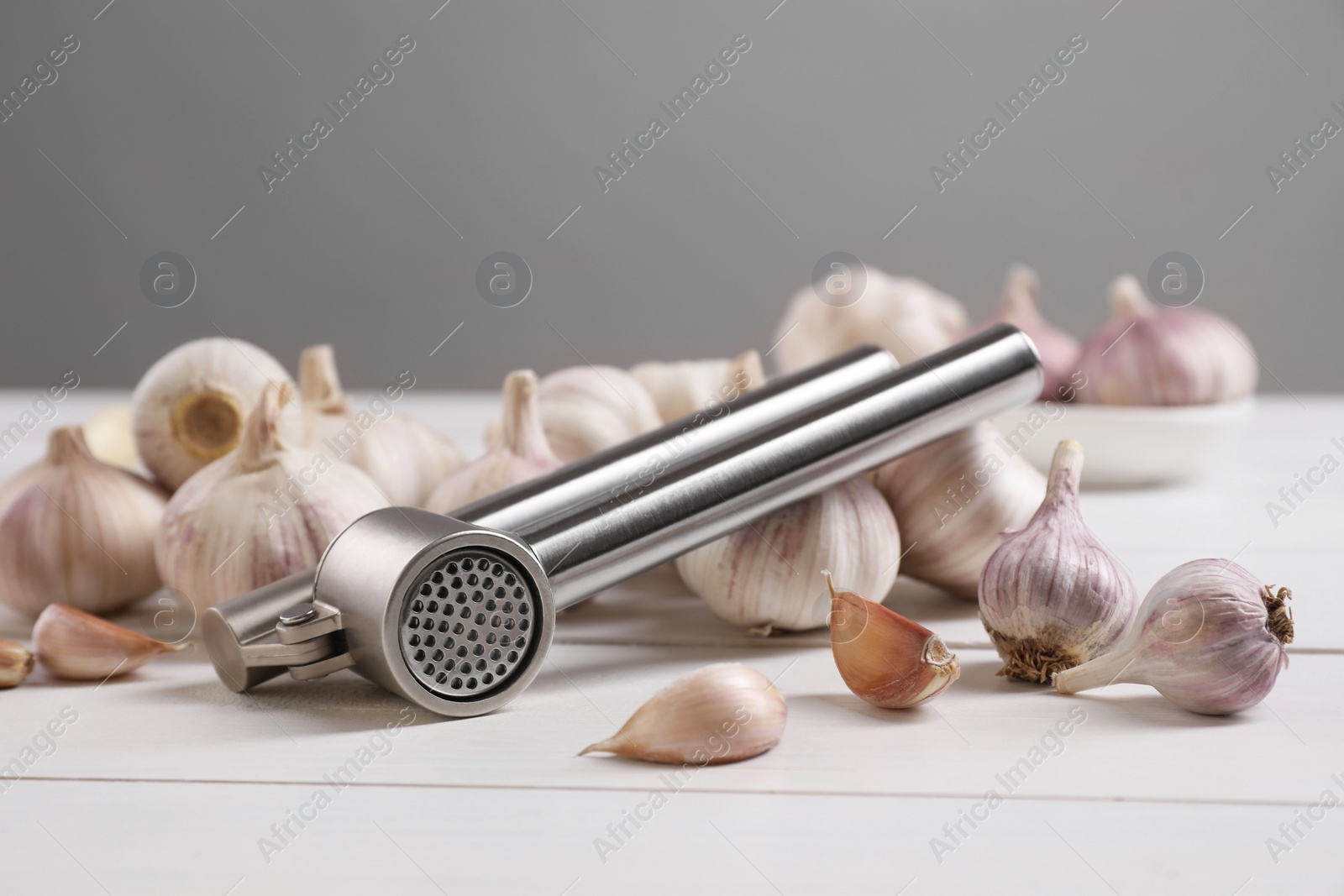 Photo of Metal press and garlic on white table, closeup