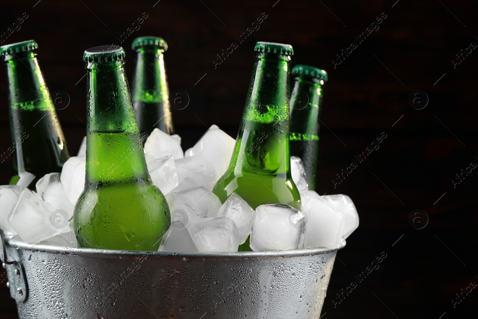 Photo of Metal bucket with bottles of beer and ice cubes on dark background, closeup