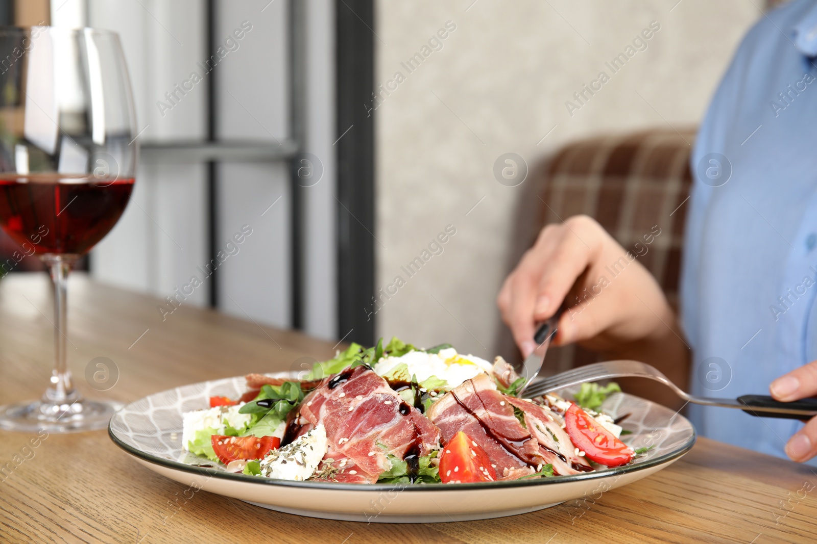 Photo of Woman eating delicious prosciutto salad at wooden table indoors, closeup. Space for text