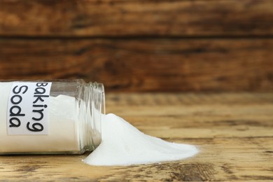 Photo of Overturned jar with baking soda on wooden table, closeup. Space for text