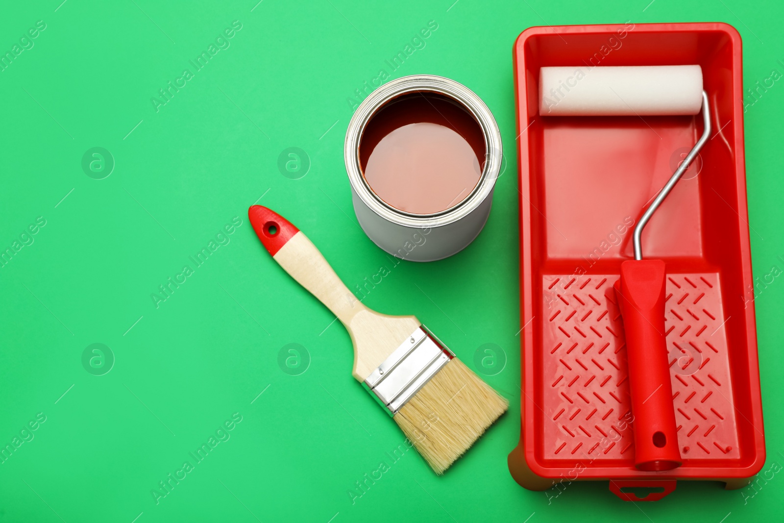 Photo of Can of orange paint, brush, roller and container on green background. Space for text