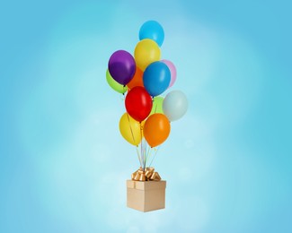 Many balloons tied to gift box on light blue background