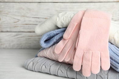 Photo of Stacked sweaters and gloves on wooden table, closeup. Autumn clothes