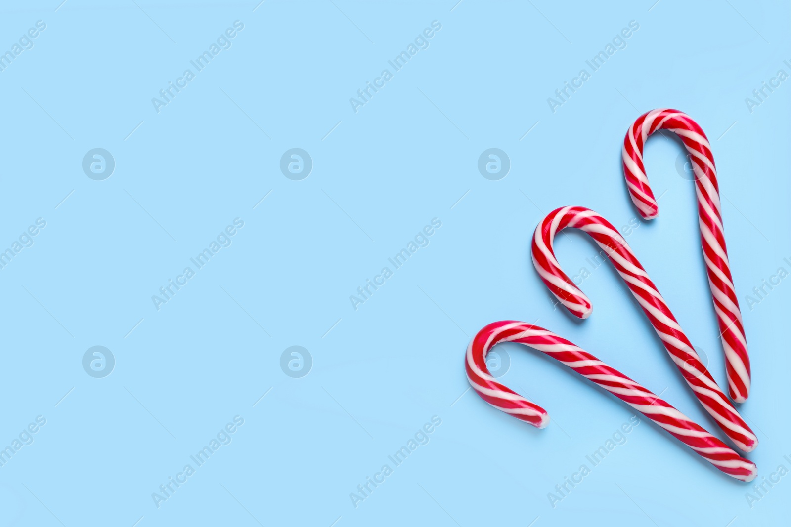 Photo of Sweet Christmas candy canes on light blue background, flat lay. Space for text