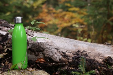 Photo of Green thermo bottle near log in forest
