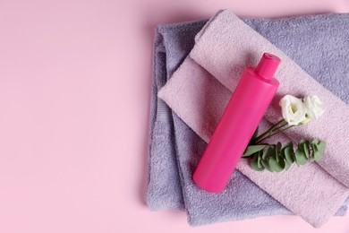 Photo of Soft folded towels with flowers, eucalyptus branch and cosmetic product on pink background, top view. Space for text