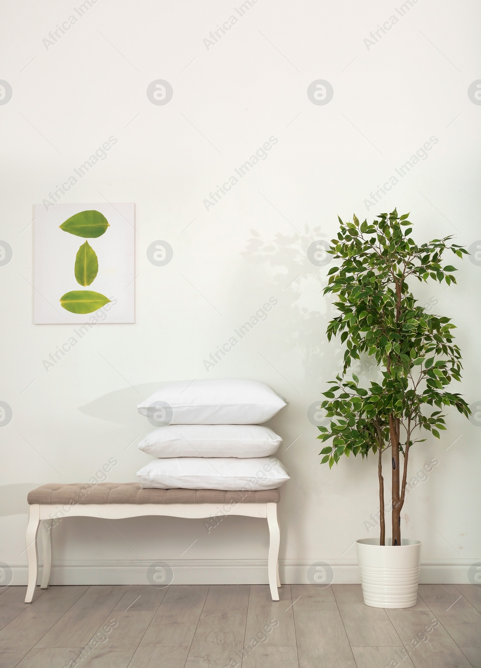 Photo of Pile of soft bed pillows on ottoman near wall in room