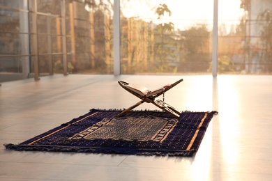 Photo of Rehal with open Quran and Muslim prayer beads on rug indoors