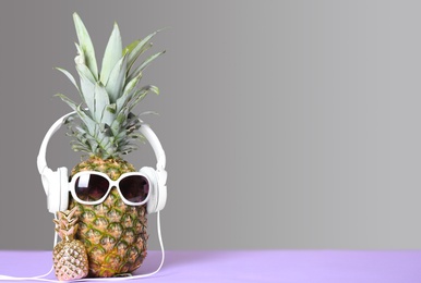 Photo of Pineapple with headphones and sunglasses on table against grey background. Space for text