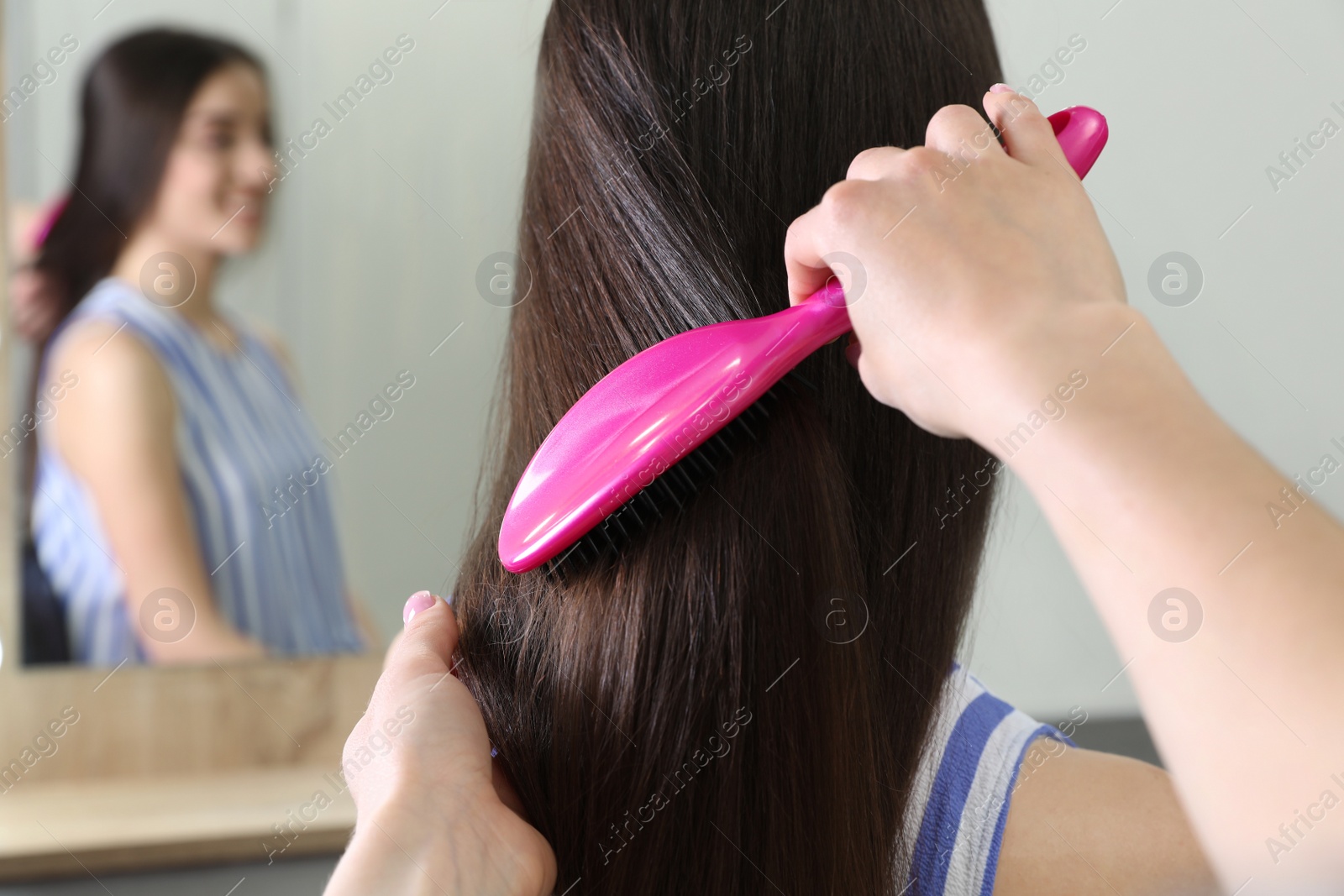 Photo of Woman combing friend's hair with cushion brush indoors, closeup