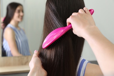 Woman combing friend's hair with cushion brush indoors, closeup