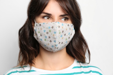 Young woman in protective face mask on light background, closeup