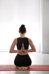 Photo of Woman practicing vajrasana with namaste behind back in yoga studio