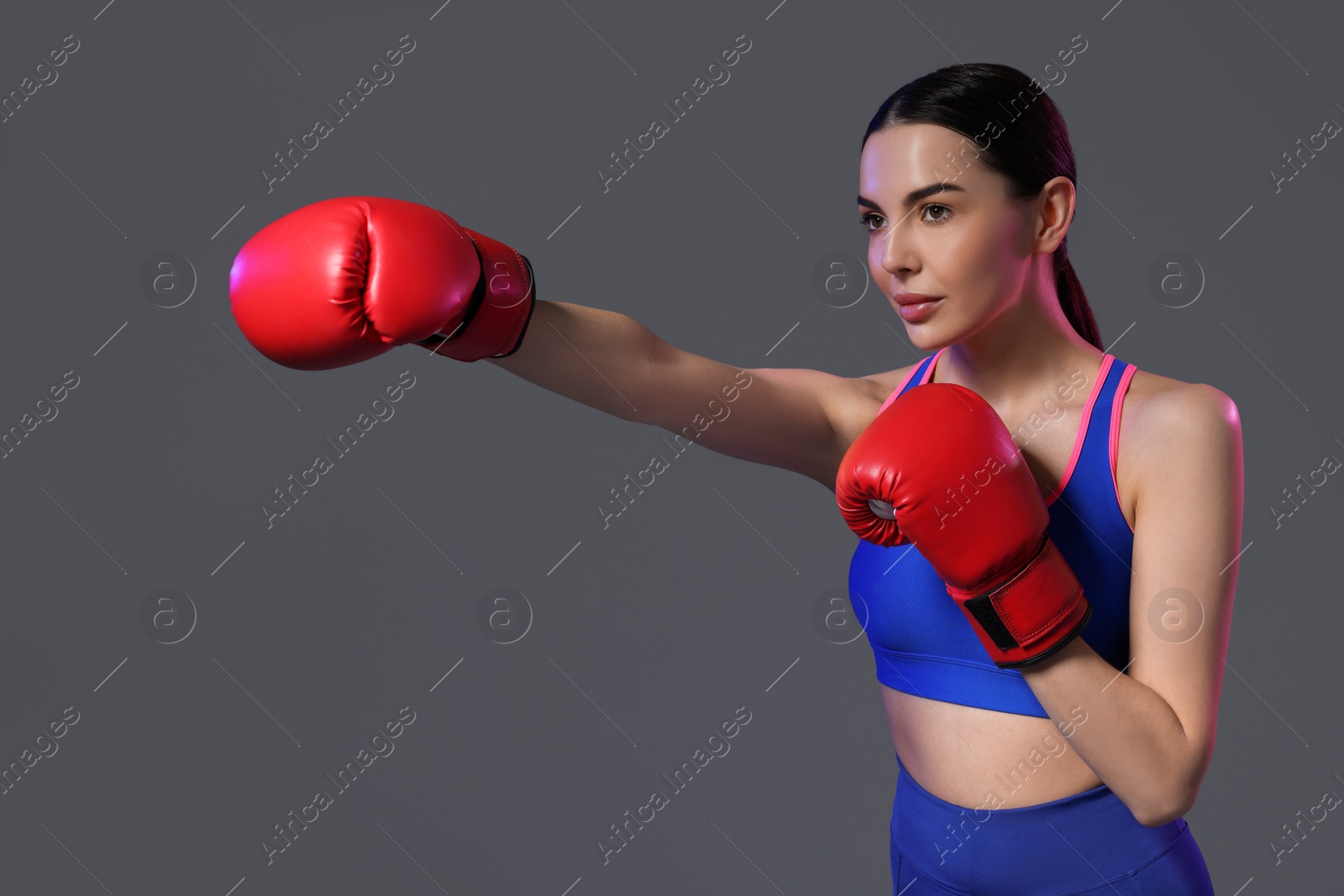 Photo of Beautiful woman wearing boxing gloves training in color lights on grey background