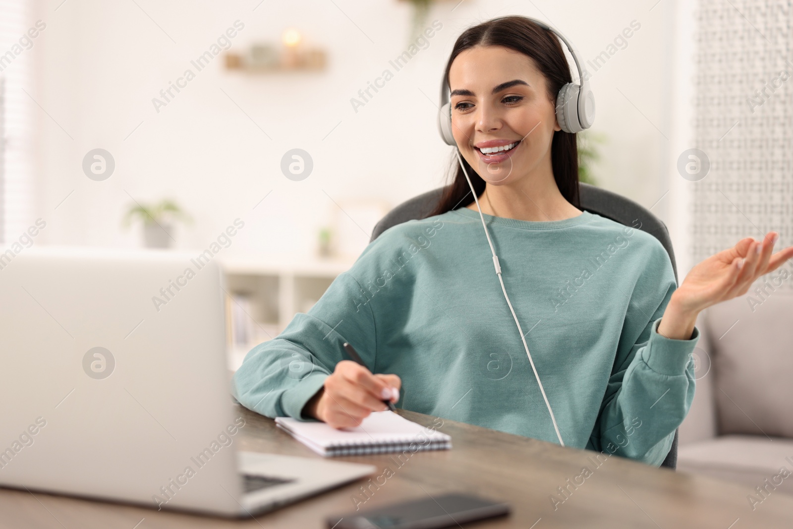 Photo of Young woman in headphones using video chat during webinar at table in room