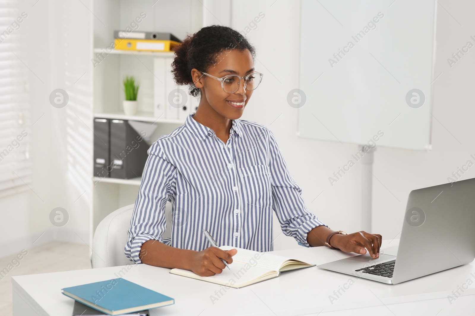 Photo of Smiling African American intern working at white table in office