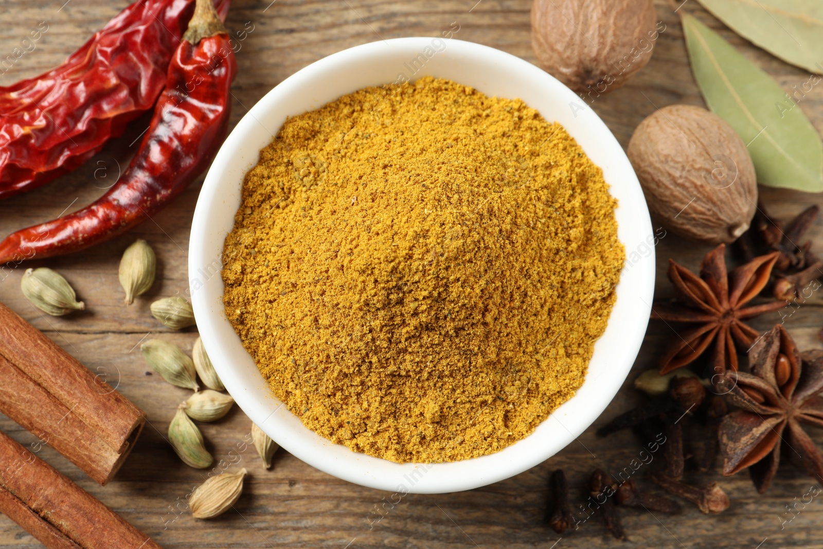 Photo of Dry curry powder in bowl surrounded by other spices on wooden table, flat lay