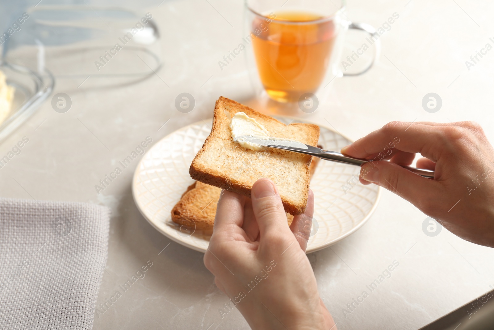 Photo of Woman spreading butter on toasted bread at table, closeup