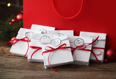Photo of Set of gifts near red bag on wooden table, closeup. New Year advent calendar
