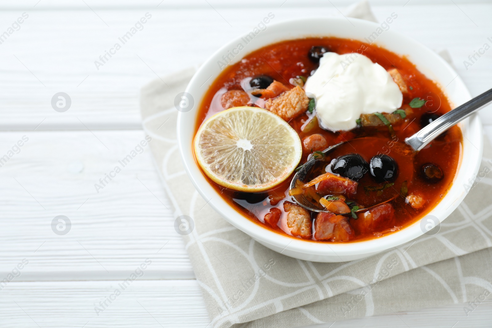 Photo of Meat solyanka soup with sausages, olives, vegetables and spoon on white wooden table, closeup. Space for text