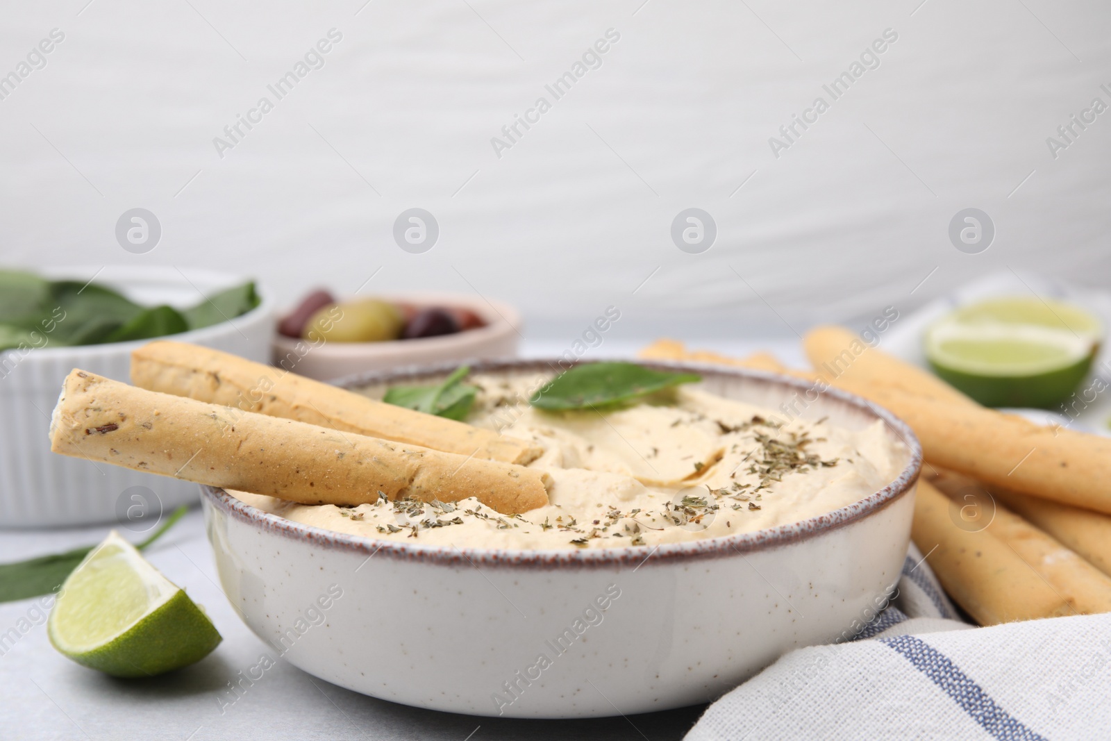 Photo of Delicious hummus with grissini sticks on light grey table, closeup