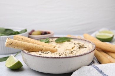 Delicious hummus with grissini sticks on light grey table, closeup