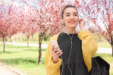 Photo of Young woman using phone for listening to music outdoors