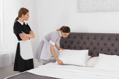 Professional chambermaids making bed in hotel room