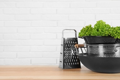 Photo of Set of clean cookware and lettuce on table against  white brick wall. Space for text