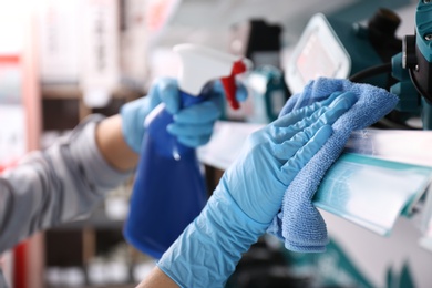 Photo of Woman cleaning shelf with rag and detergent in store, closeup