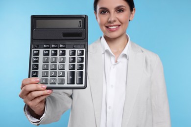 Photo of Smiling accountant against light blue background, focus on calculator