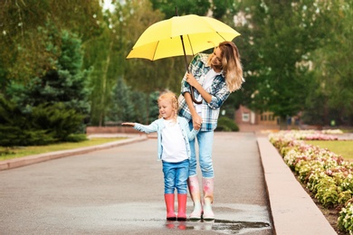 Happy mother and daughter with umbrella under rain in park