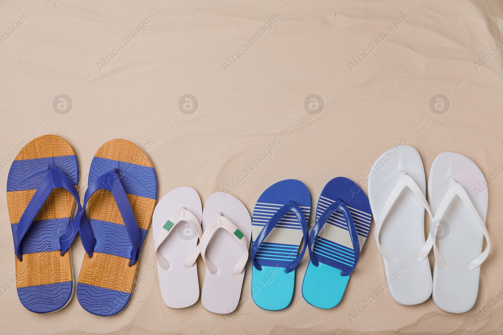 Photo of Different bright flip flops on sand, flat lay. Space for text