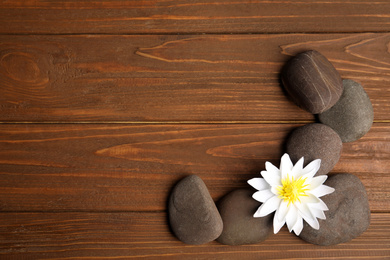 Photo of Stones with lotus flower and space for text on wooden background, flat lay. Zen lifestyle