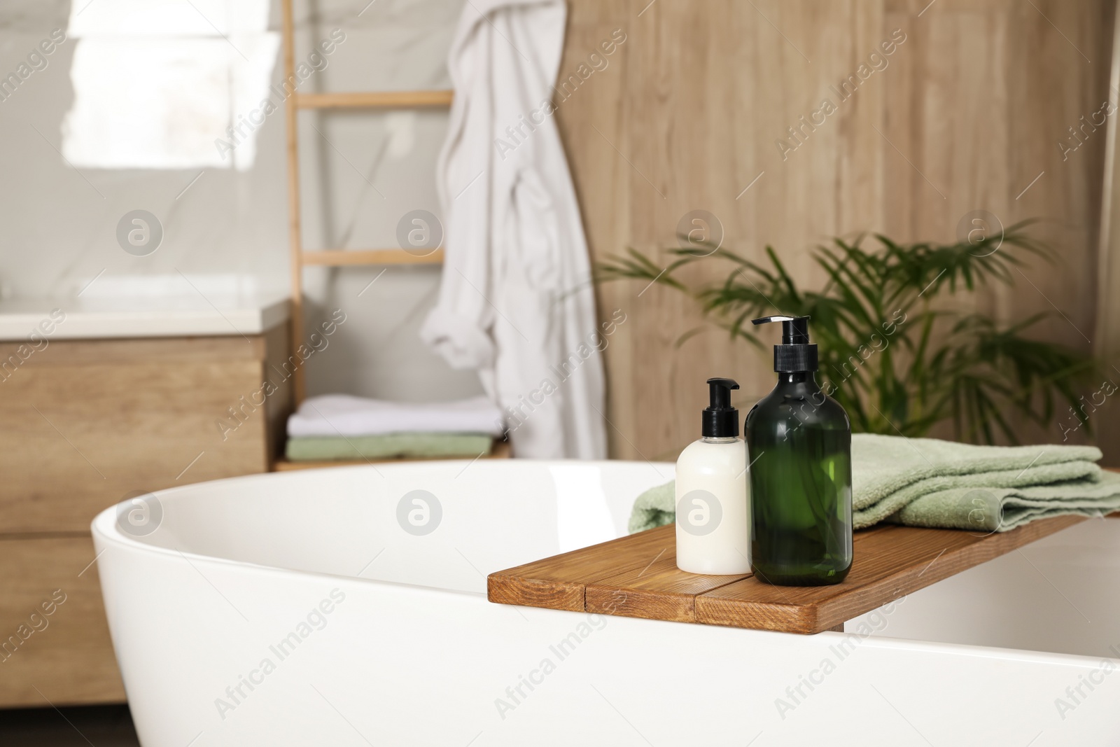 Photo of Wooden bath tray with bottles of shower gels and towel on tub indoors, space for text